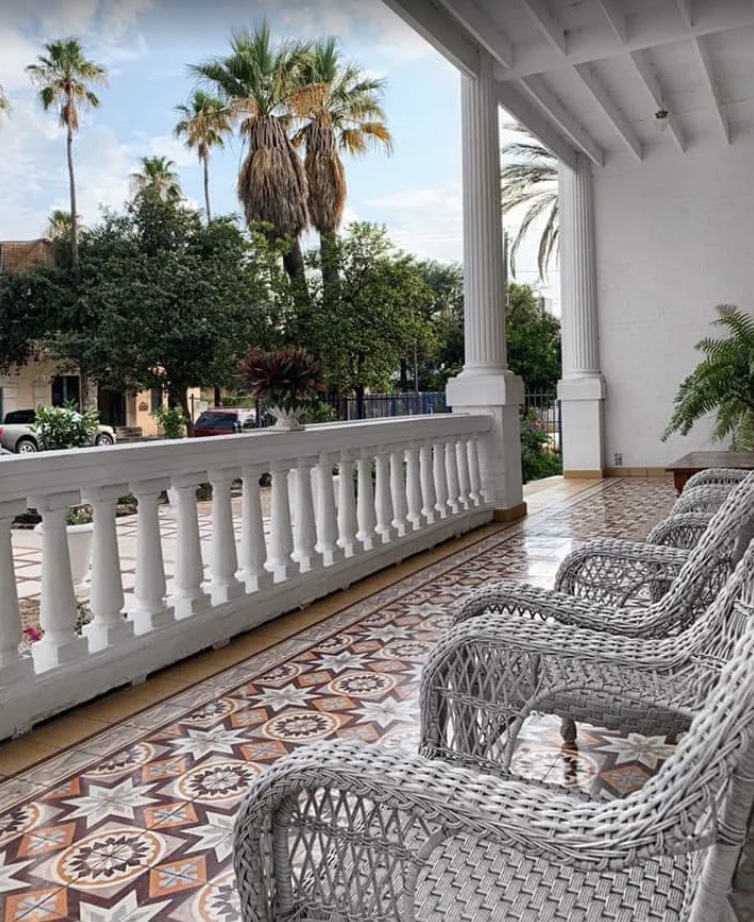 Wicker armchairs on the mansion's tiled front porch, looking out over white balustrades and palm trees